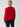 A person with blonde hair styled in a bun is wearing the Cable Mock Neck Sweater in Mars Red by Sanctuary Clothing, paired with black pants. They are facing away from the camera against a solid, light gray background.