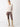 A person is posing in a Cozy V Back Sweater Coco Smoke Multi by Sanctuary Clothing, along with brown leather pants and beige knee-high boots against a plain, light background. They are standing with their hands behind their back, looking directly at the camera.