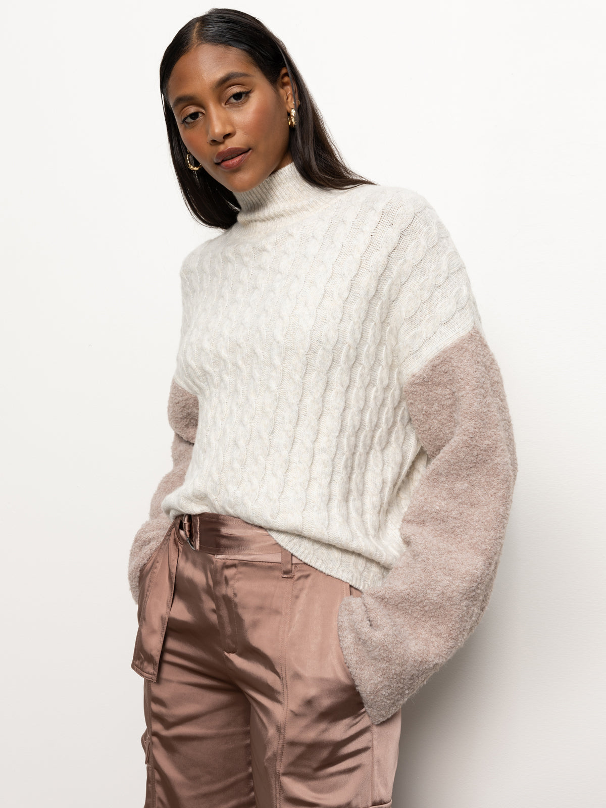 A person with long hair is wearing Sanctuary Clothing's boucle sleeve sweater in light heather oatmeal multi, paired with silky beige pants, and standing against a plain white background.