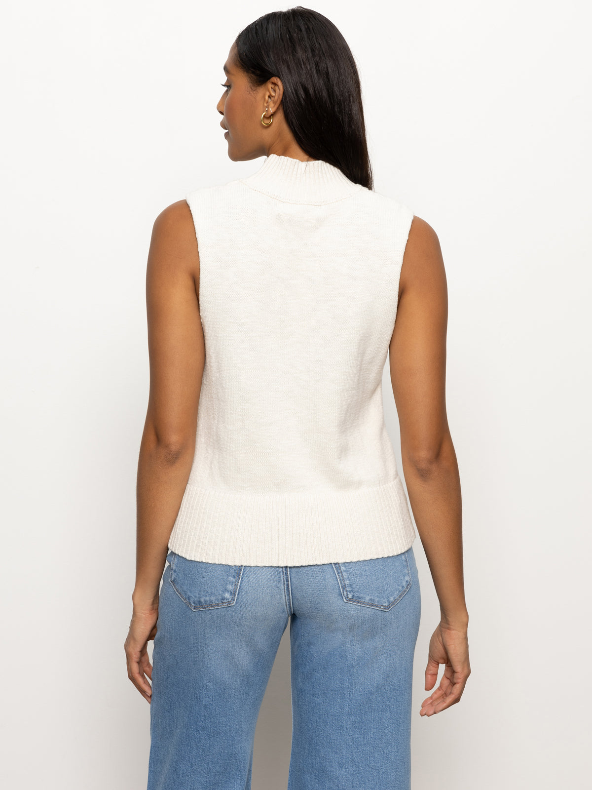 A rear view of a person with long dark hair is shown wearing Sanctuary Clothing's "rib detail mock tank" in light oat, paired with light blue jeans, against a plain background.