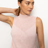 A person with long hair tied back is wearing the "rib detail mock tank rosewood" by Sanctuary Clothing, a sleeveless knit top with light pink hues and a mock turtleneck. They are gazing to the side against a plain white background.