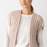 A person is wearing the chunky sweater vest in rosewood marl from Sanctuary Clothing over a white ribbed shirt, teamed with blue jeans. They are standing against a plain white background and looking towards the camera.