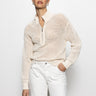 A person with short hair is wearing Sanctuary Clothing's open knit 1/2 zip sweater in eco natural and white pants. They stand against a plain white background, looking at the camera with a neutral expression.