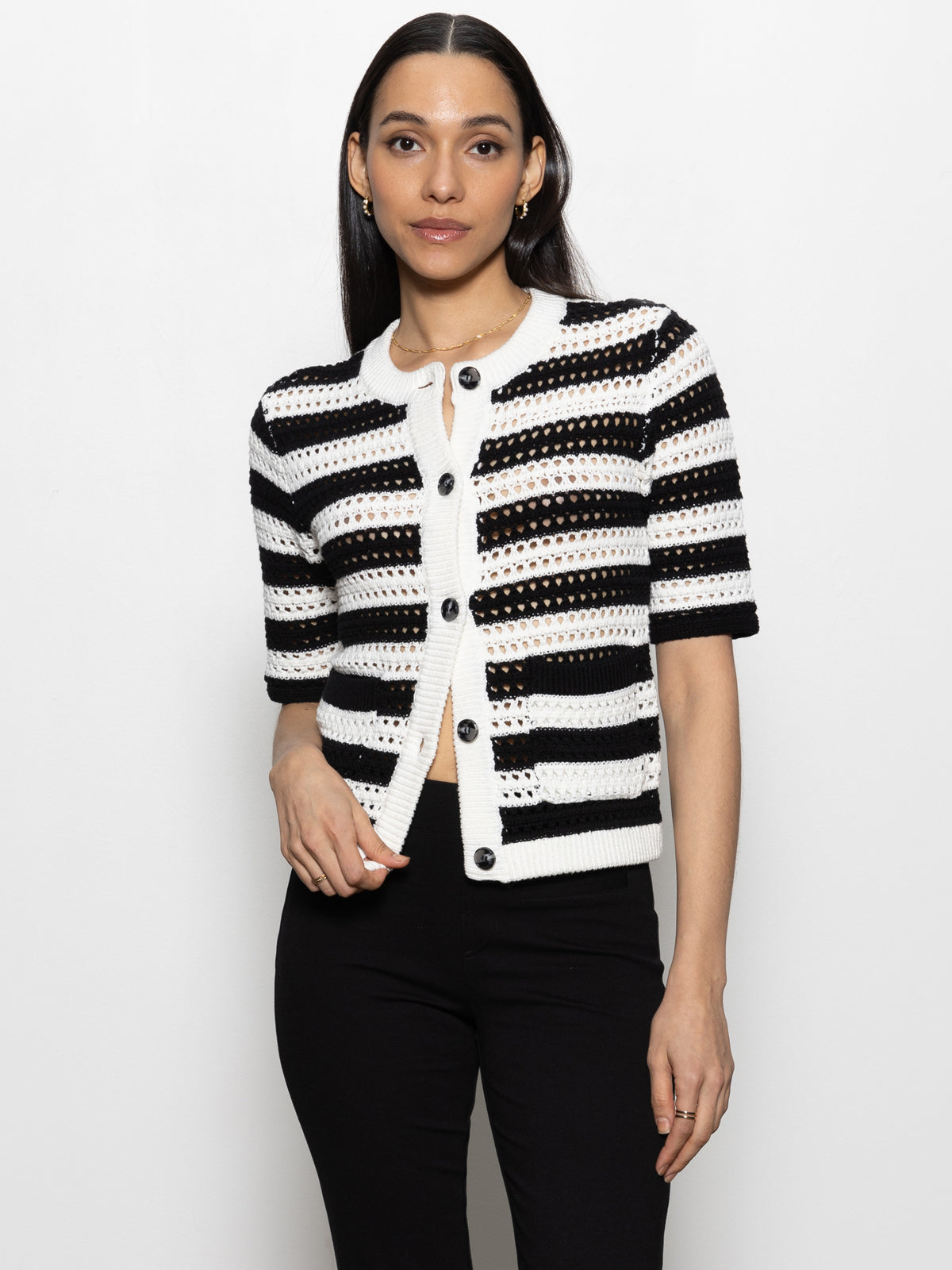 A person with long dark hair models the Sanctuary Clothing open knit sweater jacket in chalk black stripe against a plain white background, paired with black pants.