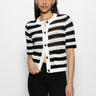 A person with long dark hair models the Sanctuary Clothing open knit sweater jacket in chalk black stripe against a plain white background, paired with black pants.