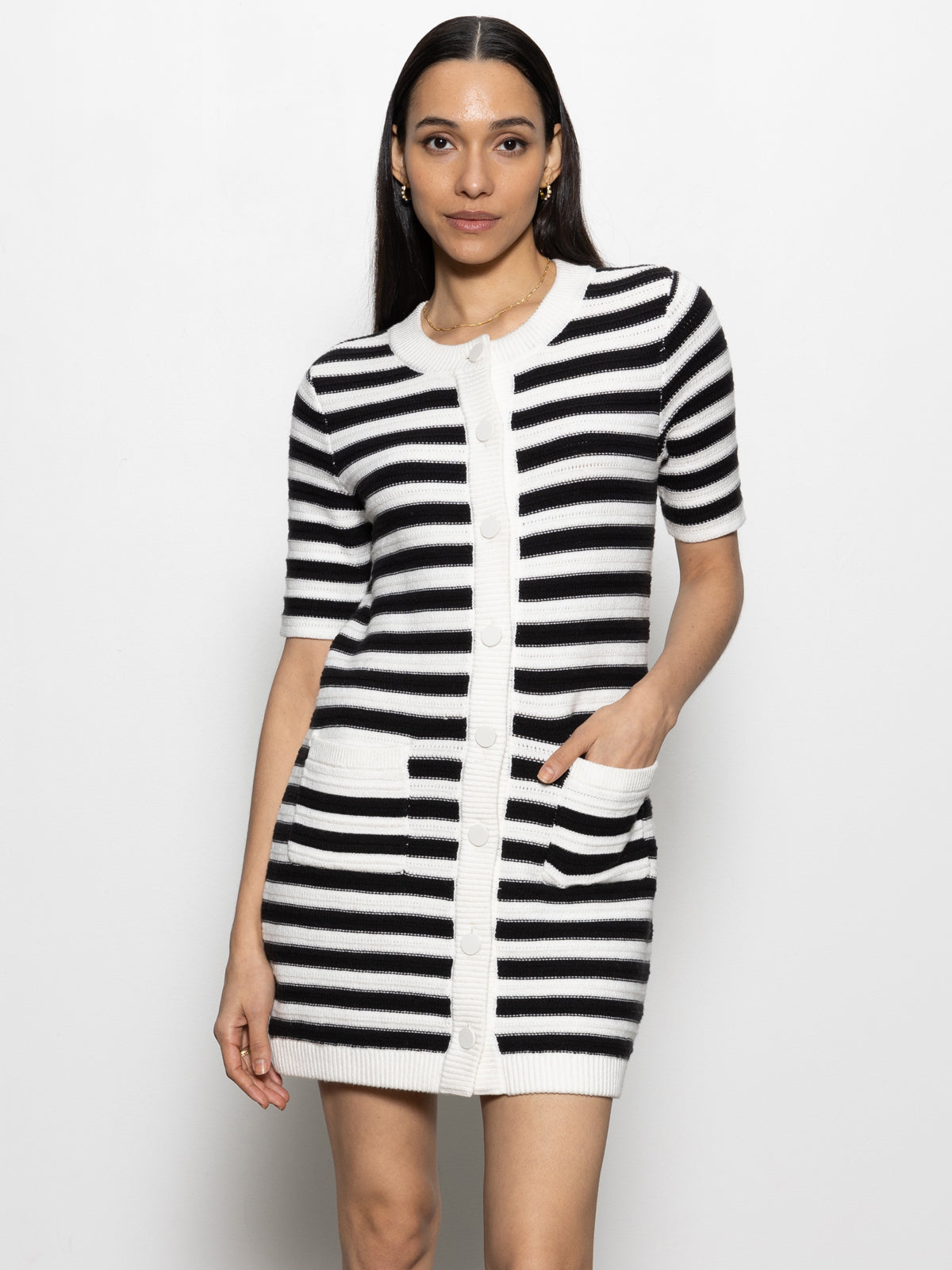 A woman wears the Sanctuary Clothing button front knitted dress in chalk and black stripe, featuring a round neckline, short sleeves, and front pockets. She stands against a plain white background.