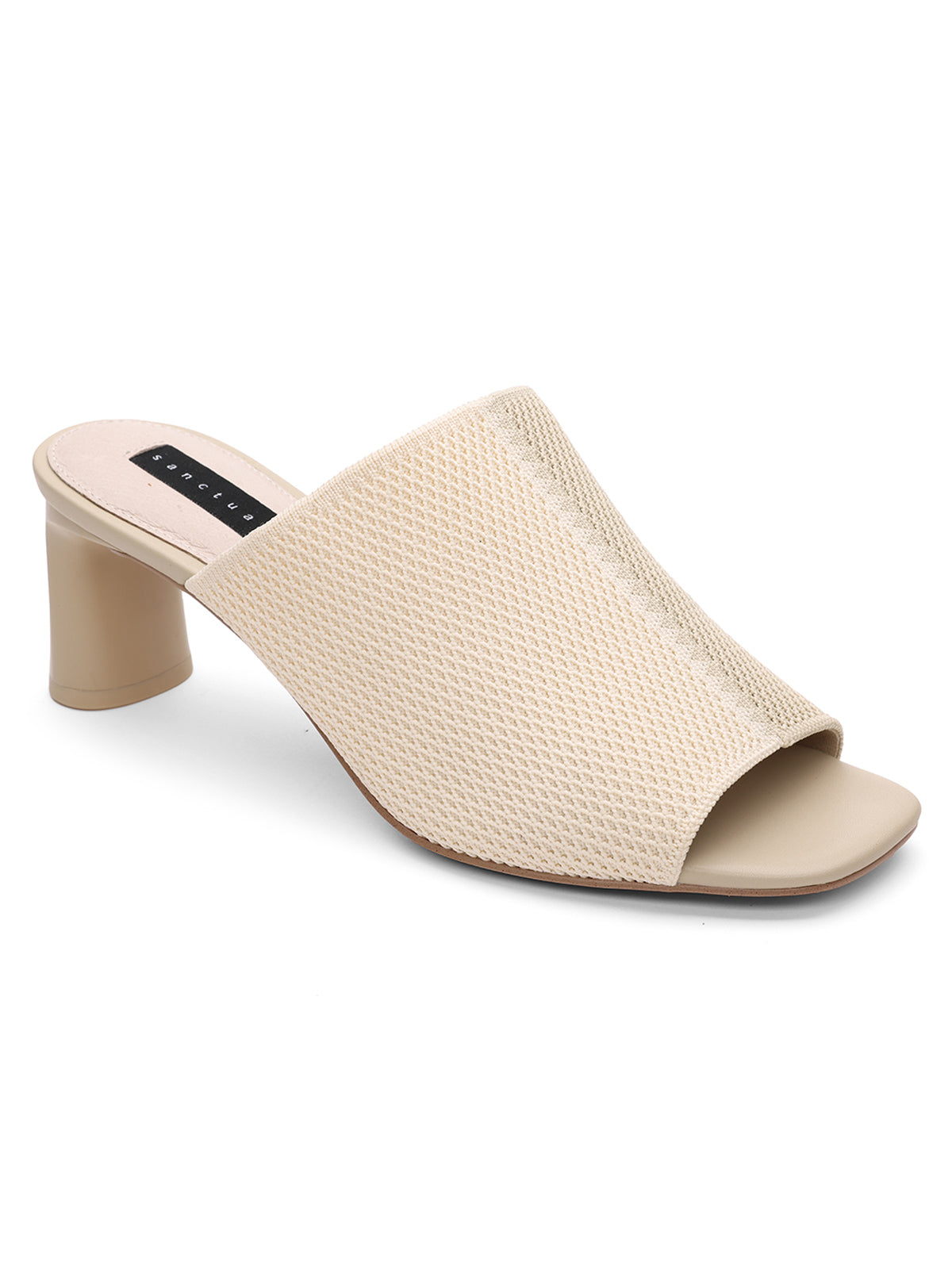 The Behold Sandal Milk Birch by Sanctuary Clothing is a beige open-toe mule featuring a block heel and a textured fabric upper. It has a moderately high heel and exudes a minimalist design. The interior sole is crafted in a lighter shade, offering an elegant contrast to the textured exterior.