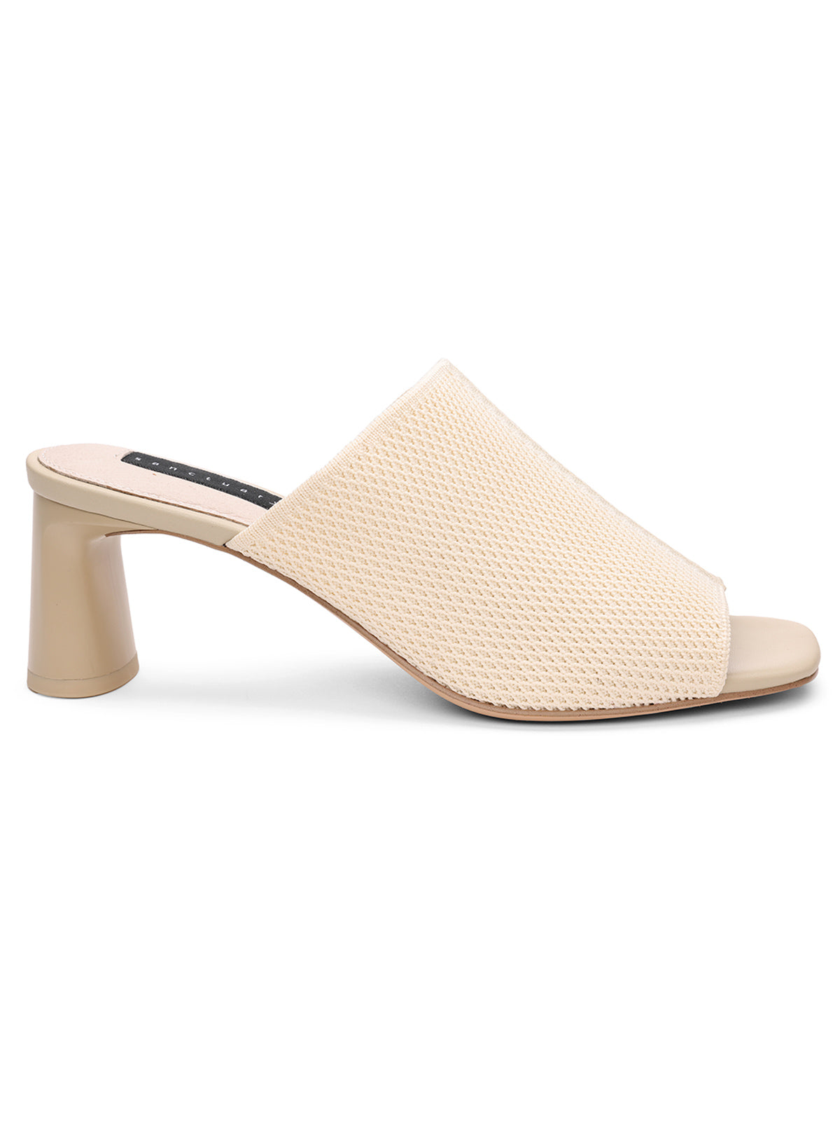 The Behold Sandal Milk Birch by Sanctuary Clothing is a beige open-toe mule featuring a textured upper and a wide mid-heel. The insole is made of a soft material with a contrasting black strip near the heel area, showcasing a minimalist and elegant design.