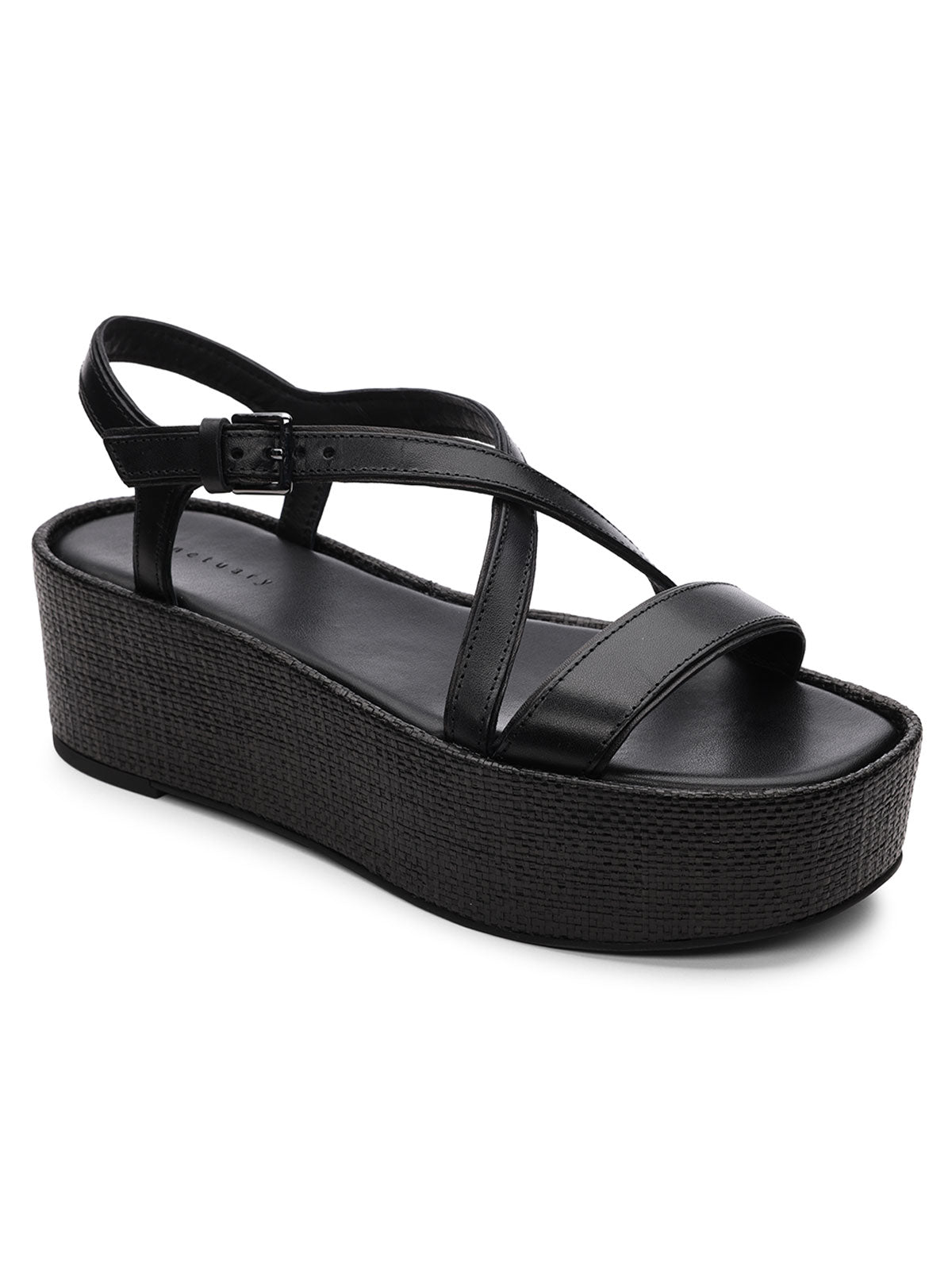 The Define Sandal Black Black by Sanctuary Clothing is a black wedge sandal featuring a wide toe strap and a crisscross ankle strap with a buckle. It has a thick sole with a textured pattern, offering both minimalist design and comfort.