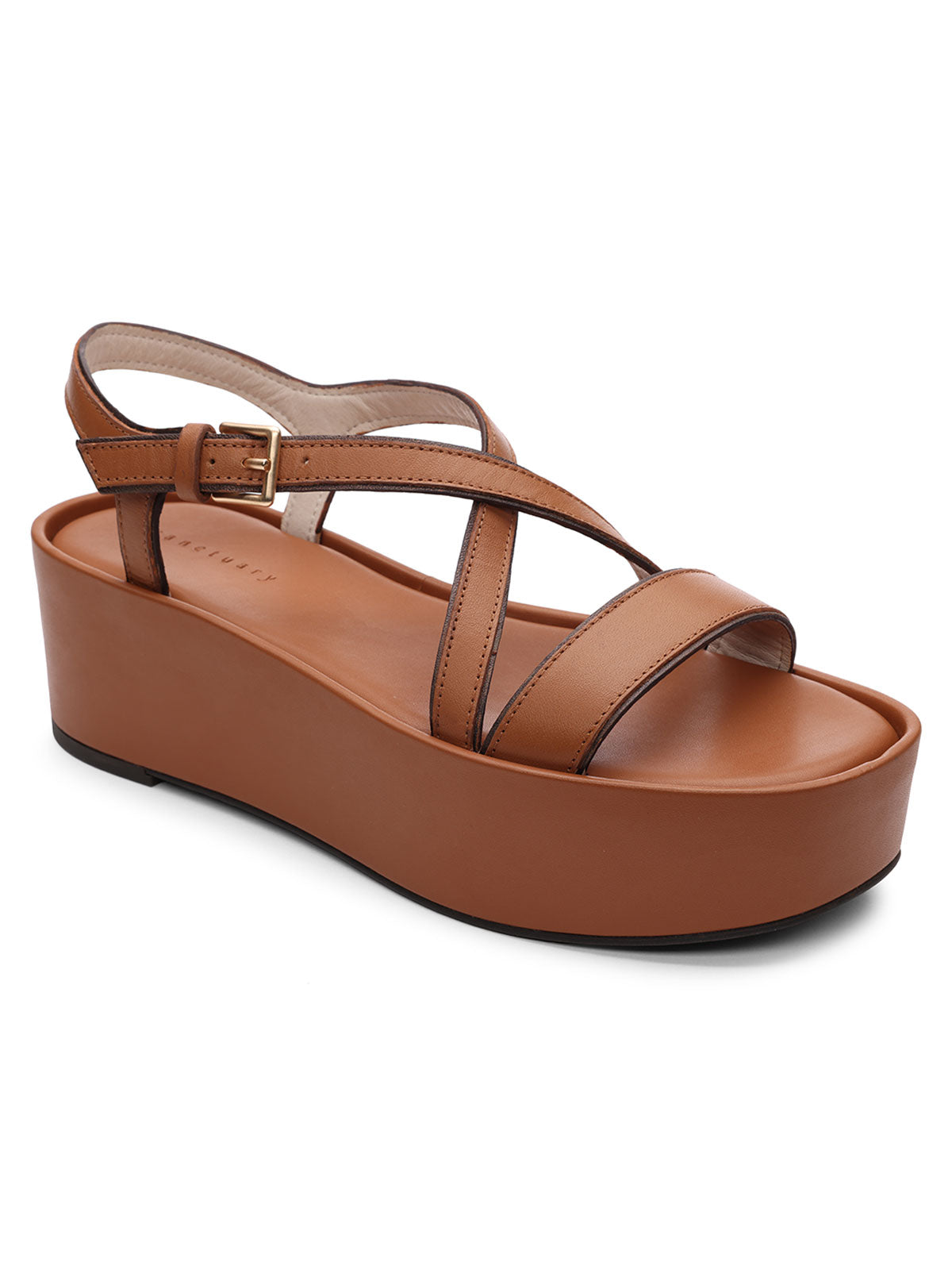 The Define Sandal Deep Honey by Sanctuary Clothing is a single platform sandal in a tan brown hue featuring a thick sole, closed heel, and crisscross straps. It also includes an adjustable ankle strap with a gold buckle and boasts a cushioned footbed for added comfort.