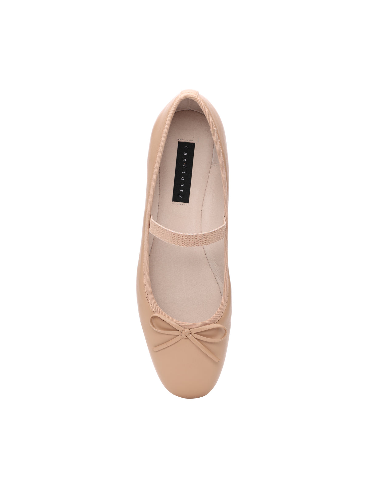 Top-down view of the Facile Ballet Flat Nude by Sanctuary Clothing, featuring a small bow at the toe and an elastic strap across the middle. The interior has a white lining and a black insole tag with text. The background is white, making the shoe the focal point of the image.