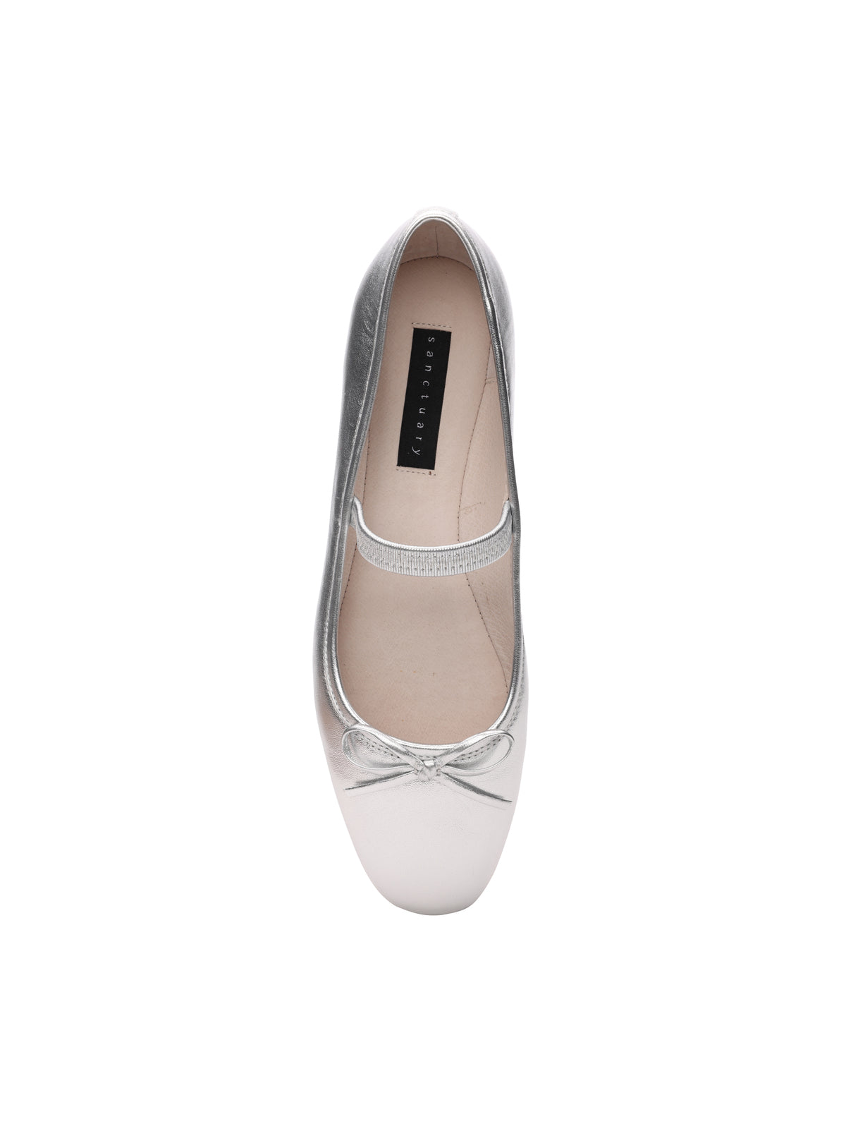 Top view of a single Facile Ballet Flat Silver shoe by Sanctuary Clothing, featuring a strap across the instep and a small bow at the toe. The inside of the shoe is beige with a black label inscribed with "AERIN LUXE." The design is sleek and elegant.