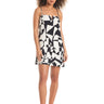 A person stands barefoot, draped in the Abstract Island Dress White Sand by Sanctuary Clothing. The dress features a black and white abstract pattern with thin straps. They have curly hair and a neutral expression, posing against a plain white background.