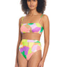 A person with curly hair is wearing a vibrant Daytripper High Rise Bikini Bottom Multi from Sanctuary Clothing, featuring a colorful camouflage pattern with hues of pink, yellow, green, and purple. The set includes a high-waisted bottom and a square-neck top against a white background.