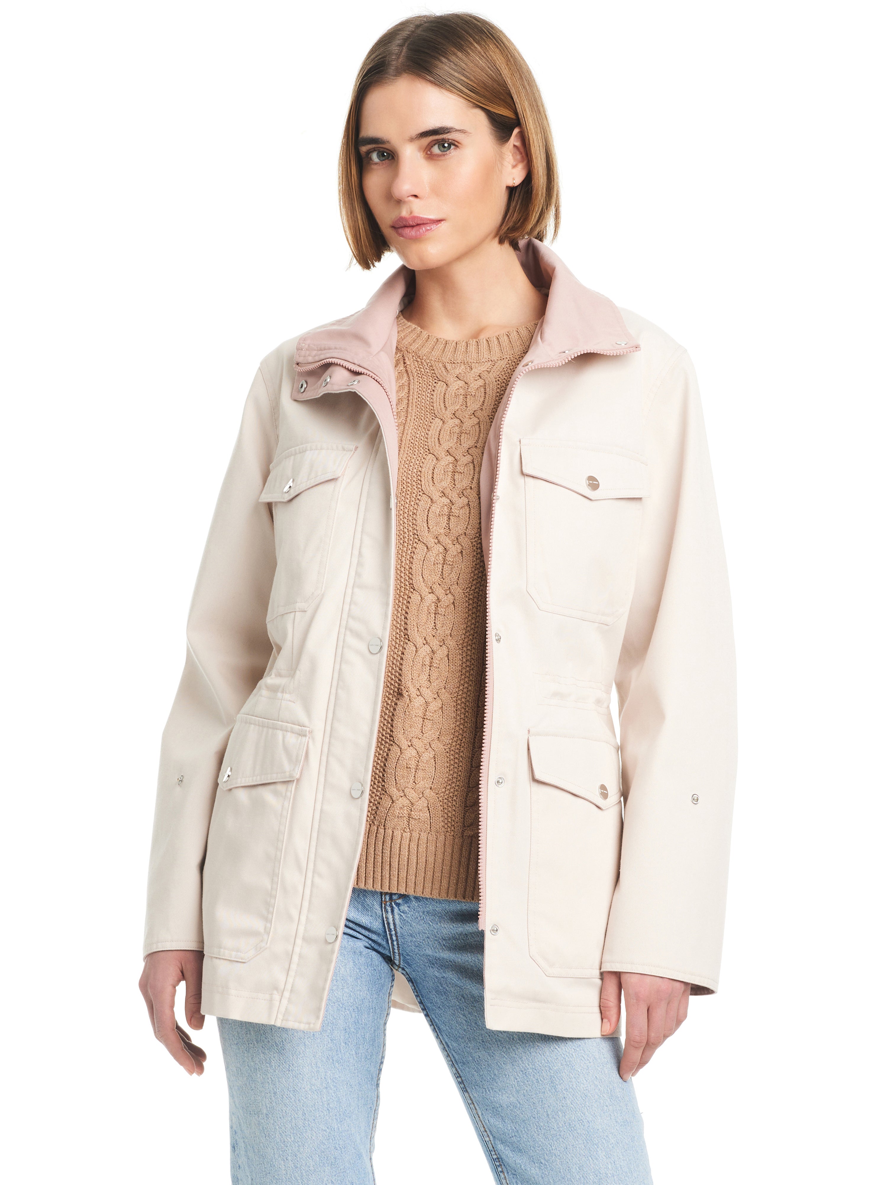 A woman with short brown hair is wearing the Cotton Touch Relaxed Twill Jac Moonbeam by Sanctuary Clothing, featuring multiple pockets, over a tan cable-knit sweater and light blue jeans. She stands against a white background, looking forward with a neutral expression.