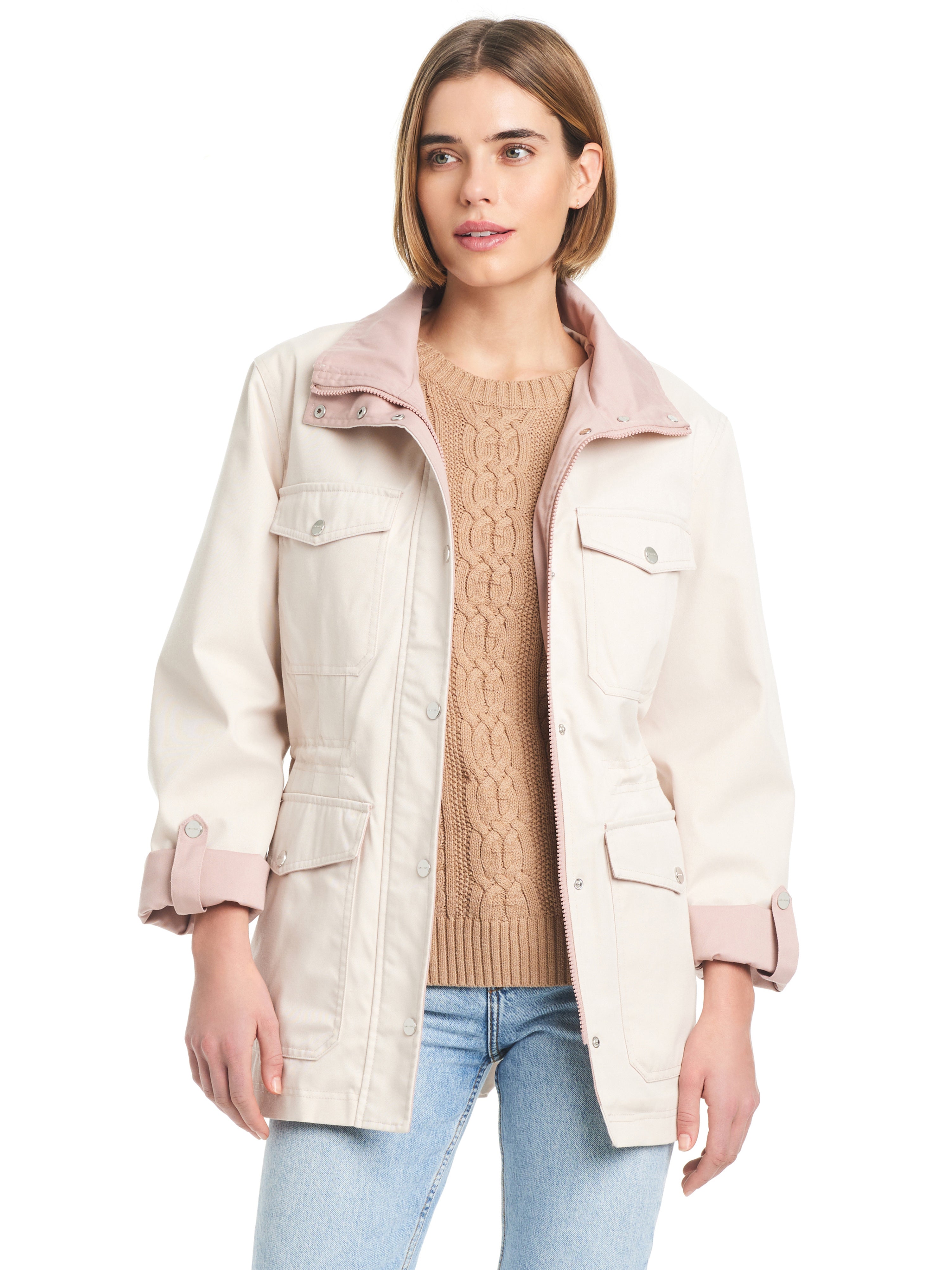 A woman with shoulder-length hair is wearing a Sanctuary Clothing Cotton Touch Relaxed Twill Jac Moonbeam jacket, a beige cable knit sweater, and light blue jeans. She is standing against a white background, looking slightly to the side with a neutral expression.