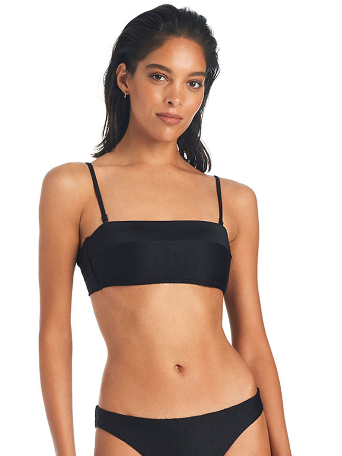 A woman wearing the "On The Water Texture Bandeau Bikini Top Black" by Sanctuary Clothing stands against a white background. The bikini top is a bandeau style, and the bottoms are high-cut. She has shoulder-length dark hair and a neutral expression.