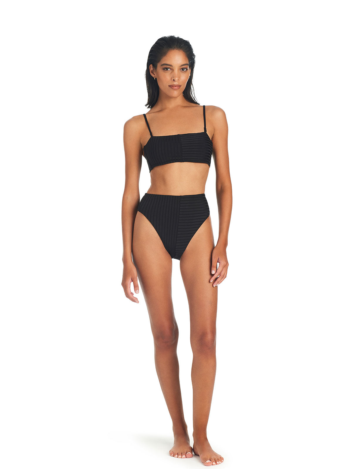 A woman stands against a white background wearing the Refresh Rib Bandeau Bikini Top in black from Sanctuary Clothing. The bikini top features thin straps and a square neckline, while the bottoms are high-waisted. She has long dark hair and a neutral expression.