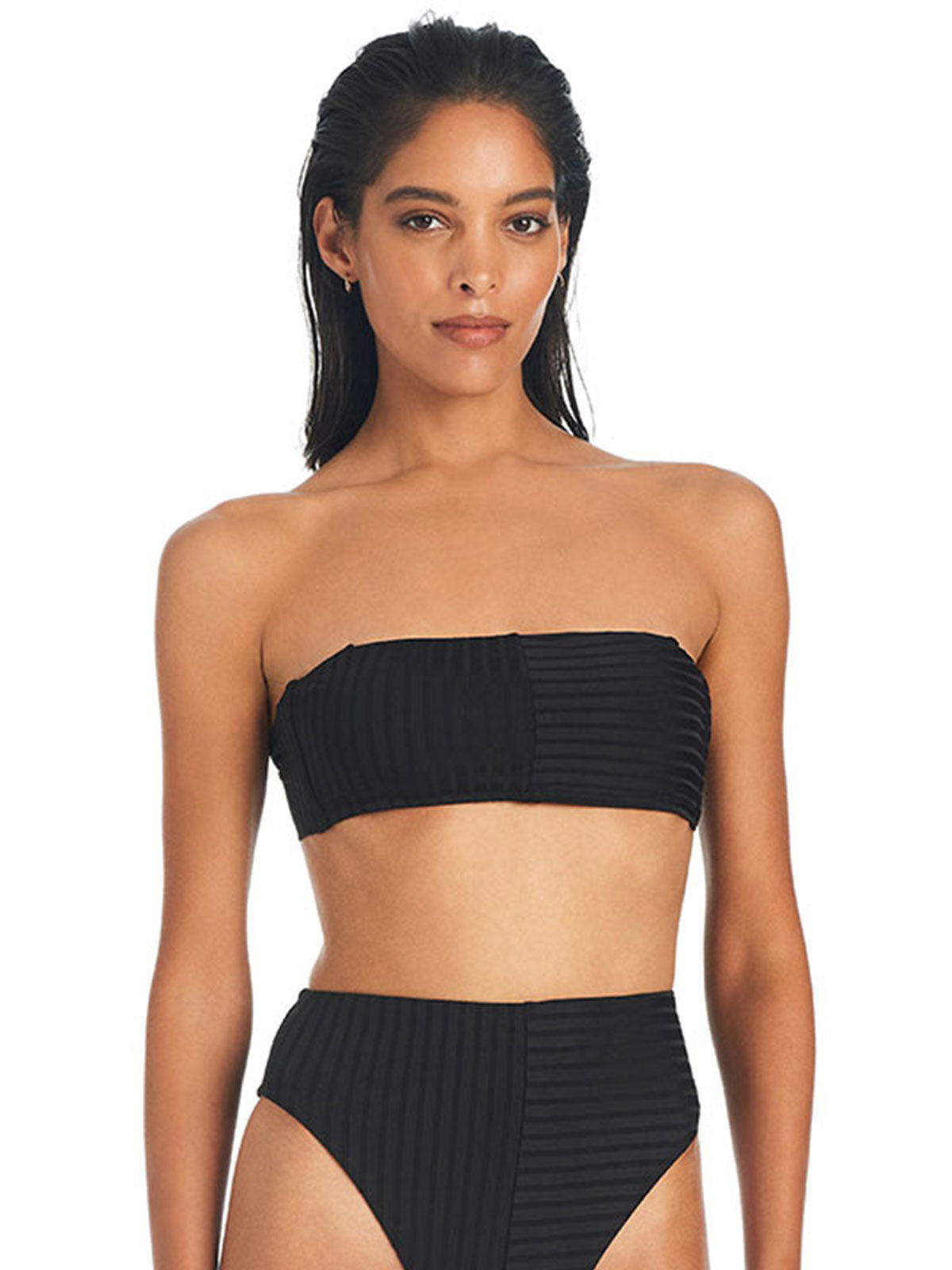 A woman with straight, dark hair is wearing the Refresh Rib Bandeau Bikini Top in black from Sanctuary Clothing, paired with high-waisted bikini bottoms. The bikini features a textured pattern with vertical stripes on one side and horizontal stripes on the other. She is standing against a plain background.