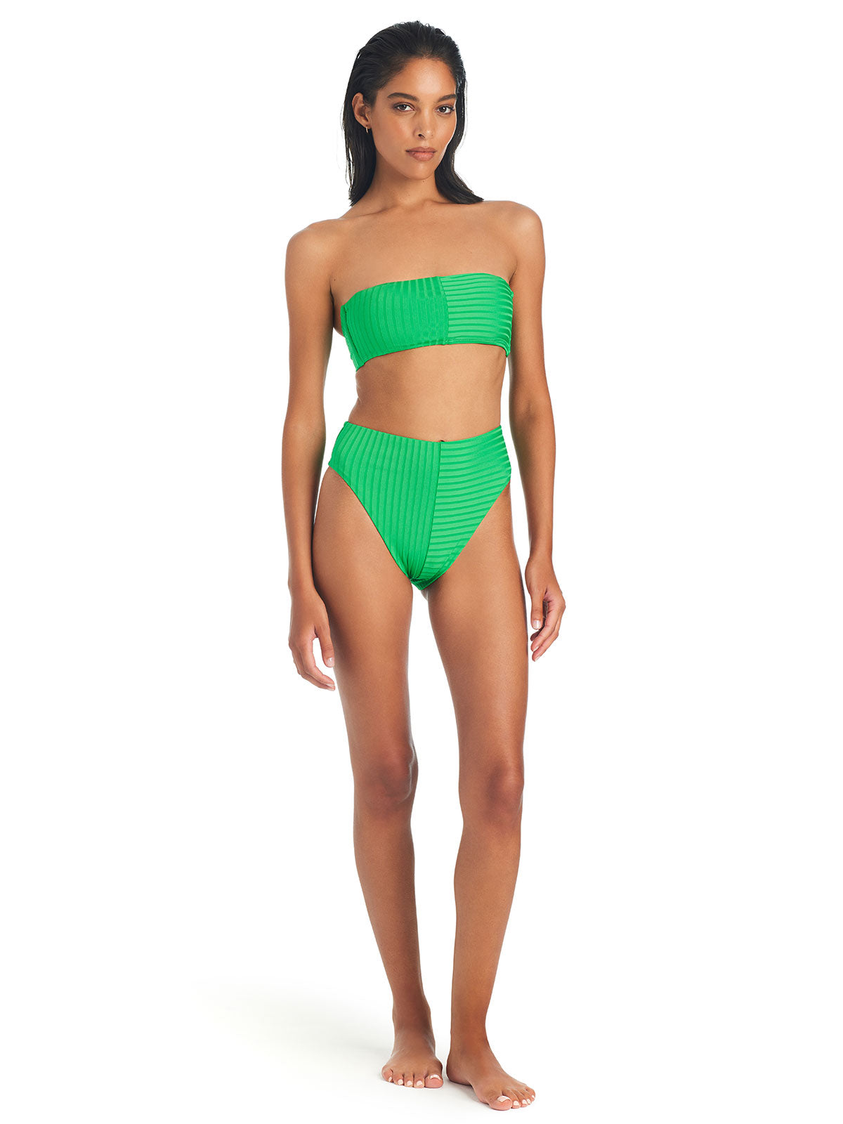 A person with long hair is wearing the Refresh Rib Bandeau Bikini Top in Green Flare by Sanctuary Clothing, along with matching high-waisted bottoms. They are standing barefoot against a white background.