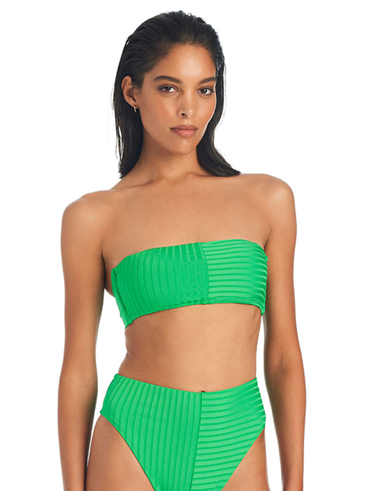 A woman is wearing the Refresh Rib Bandeau Bikini Top in Green Flare by Sanctuary Clothing, paired with high-waisted bikini bottoms. The bikini features a textured, ribbed design. She has long, dark hair that is slicked back and is standing against a plain white background, looking into the camera.