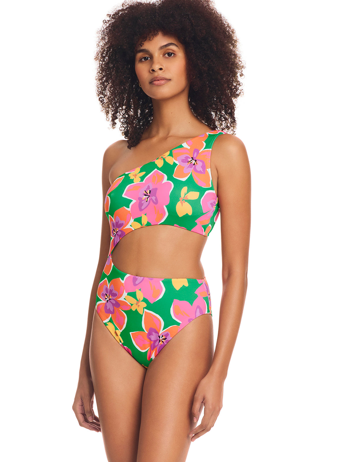 Person wearing the Super Bloom Cutout One Piece Swimsuit Multi by Sanctuary Clothing, which features a vibrant one-shoulder cutout design adorned with bold floral patterns in shades of pink, yellow, and green. The person stands confidently against a white background.