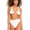 A woman with curly hair stands wearing the Sea Crochet High Rise Bikini Bottom in White Sand by Sanctuary Clothing. The top features a halter neck design with mesh detailing, and the bottoms are high-waisted. She is looking forward with a neutral expression against a plain white background.