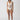 Dressed in the Sanctuary Clothing's sea crochet high leg scoop neck one piece in white sand, a person stands self-assuredly. They pair the cream-hued swimsuit, featuring a mesh panel midsection, with black and white sandals against a plain, light-colored backdrop that highlights the swimwear.