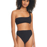 A woman with curly hair is wearing a black one-shoulder bikini top and the Sandbar Solids High Rise Bikini Bottom by Sanctuary Clothing. She is standing and looking slightly to the side against a plain white background.