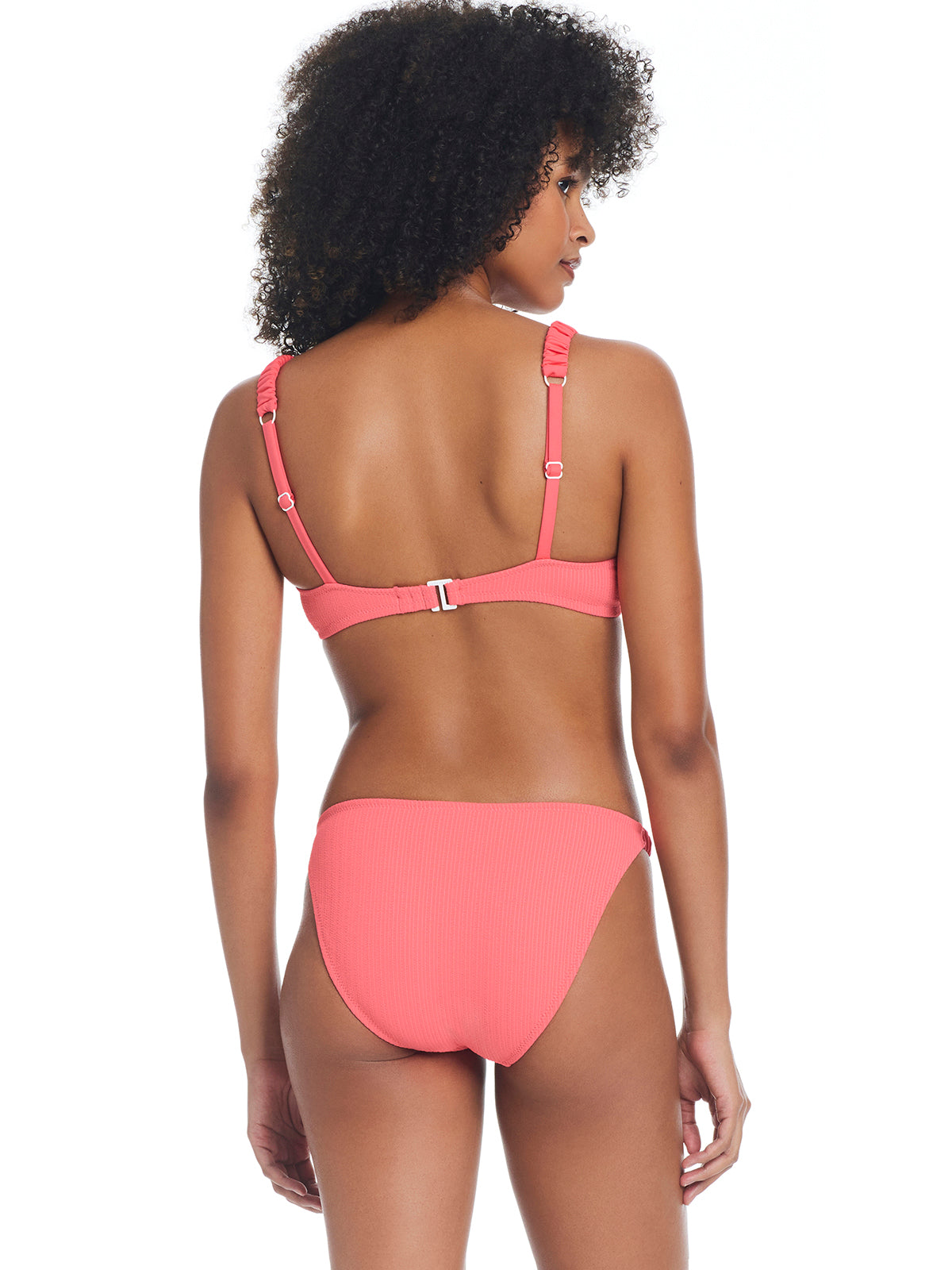 A woman with curly hair wearing the Sandbar Solids Underwire Bikini Top in Watermelon Sugar by Sanctuary Clothing. Seen from the back, the bikini top features adjustable straps and a hook closure, paired with classic cut bottoms. She stands against a white background.