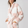 A person is wearing the Shawl Collar Teddy Robe in Rose Check by Sanctuary Clothing. They have their hands in the robe's pockets and are looking forward with a slight smile against a plain, light-colored background.