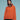 A person wearing Sanctuary Clothing's 1/4 zip cashmere-like sweater in ski orange and a black beanie with a pom-pom stands against a blue background, looking confidently into the camera. The sweater has a high collar with a half-zip.