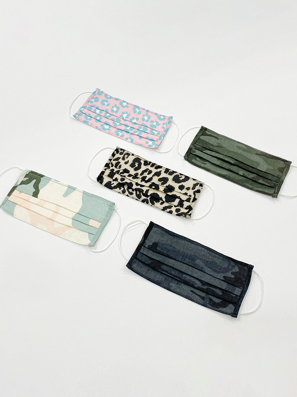 Five Lifestyle Masks from Sanctuary Clothing are spread out on a white surface. The masks feature different patterns: pink leopard print, green camouflage, black camouflage, green, and traditional leopard print. All masks have white ear loops and pleated fronts.