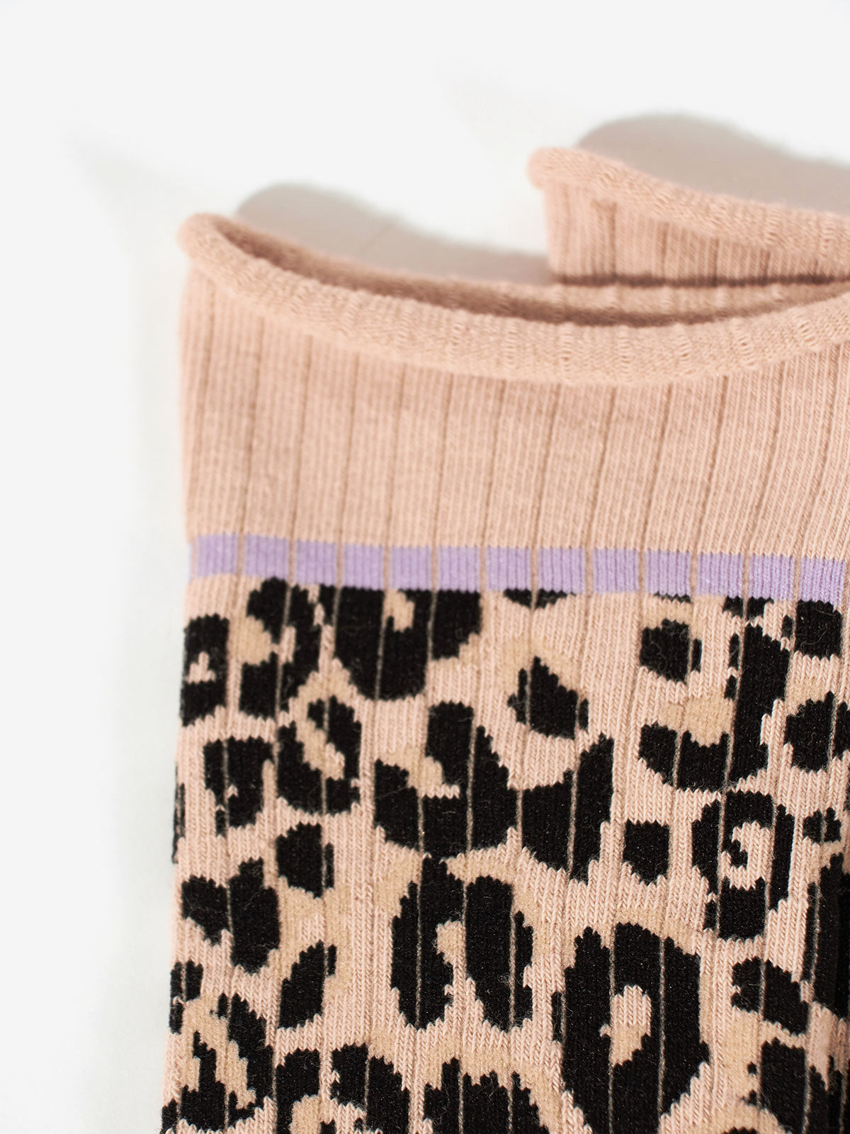 Close-up of the Classy Cat Socks by Sanctuary Clothing, showcasing a beige base with a ribbed knit cuff featuring a light purple stripe near the top. The socks are adorned with a black and light brown leopard print pattern that extends from the cuff downward.